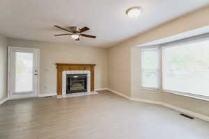 Unfurnished living room featuring ceiling fan, a fireplace, a healthy amount of sunlight, and light wood-type flooring