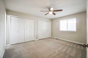 Unfurnished bedroom with ceiling fan, light carpet, and two closets