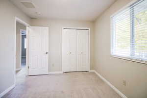 Unfurnished bedroom with a textured ceiling, a closet, light carpet, and multiple windows