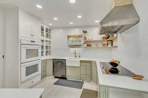 Kitchen featuring stainless steel dishwasher, double oven, sink, exhaust hood, and green cabinets