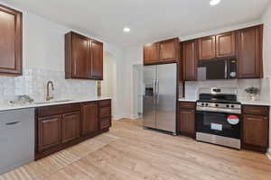 Kitchen featuring backsplash, light hardwood / wood-style floors, sink, and stainless steel appliances