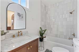 Full bathroom featuring vanity, tiled shower / bath combo, and toilet