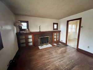 Unfurnished living room with a textured ceiling, plenty of natural light, hardwood, and a brick fireplace