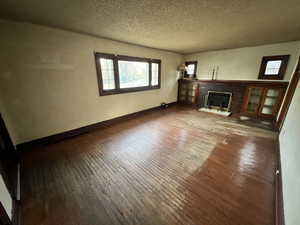 Unfurnished living room with a fireplace, wood-type flooring, and a textured ceiling and hardwood flooring