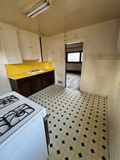 Kitchen featuring white cabinets, dark brown cabinetry, white gas range, and sink