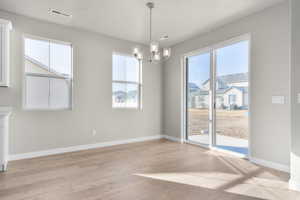 Unfurnished dining area featuring an inviting chandelier, a textured ceiling, and light wood-type flooring