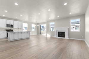 Kitchen with white cabinetry, a textured ceiling, pendant lighting, stainless steel appliances, and light hardwood / wood-style floors