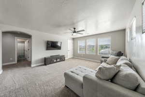 Living room featuring light carpet, arched walkways, baseboards, a textured ceiling, and ceiling fan
