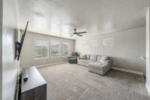 Carpeted living area with baseboards, a textured ceiling, and ceiling fan