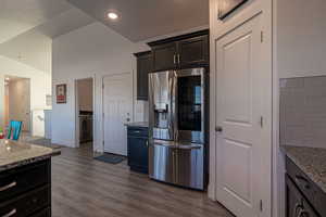 Kitchen featuring lofted ceiling, light stone counters, dark wood-type flooring, and stainless steel refrigerator with ice dispenser