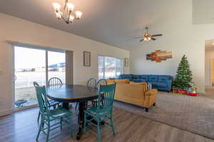 Dining area with dark hardwood / wood-style flooring, ceiling fan with notable chandelier, and lofted ceiling