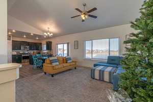 Carpeted living room with ceiling fan with notable chandelier and high vaulted ceiling