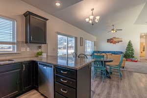 Kitchen featuring dishwasher, ceiling fan with notable chandelier, vaulted ceiling, tasteful backsplash, and light hardwood / wood-style floors