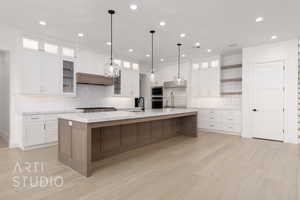 Kitchen featuring built in appliances, white cabinets, light wood-type flooring, and a large island with sink