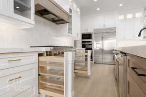 Kitchen featuring backsplash, built in appliances, light hardwood / wood-style floors, white cabinets, and custom range hood