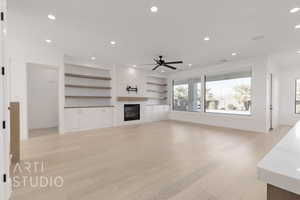 Unfurnished living room featuring built in shelves, ceiling fan, light wood-type flooring, and a fireplace