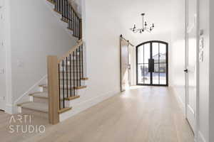 Foyer entrance with a barn door, french doors, a chandelier, and light wood-type flooring