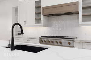 Kitchen featuring decorative backsplash, premium range hood, sink, white cabinetry, and stainless steel gas stovetop