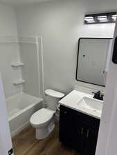 Full bathroom featuring hardwood / wood-style flooring, vanity, washtub / shower combination, and toilet