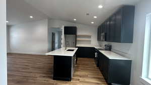 Kitchen featuring dark hardwood / wood-style flooring, sink, range with electric cooktop, vaulted ceiling, and a center island with sink