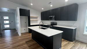 Kitchen with lofted ceiling, electric range oven, sink, light wood-type flooring, and a kitchen island with sink