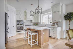 Kitchen with a center island, hanging light fixtures, stainless steel appliances, light hardwood / wood-style flooring, and a breakfast bar