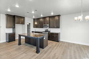 Kitchen with sink, stainless steel appliances, dark stone countertops, decorative light fixtures, and a center island with sink