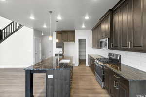 Kitchen with appliances with stainless steel finishes, sink, pendant lighting, dark stone countertops, and light hardwood / wood-style floors