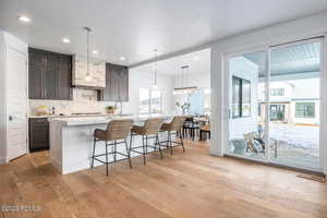 Kitchen with light wood-type flooring, dark brown cabinets, a kitchen island with sink, pendant lighting, and a breakfast bar area