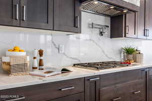 Kitchen featuring custom exhaust hood, dark brown cabinets, backsplash, and stainless steel gas cooktop