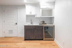 Bar featuring white cabinets, sink, wine cooler, dark brown cabinets, and light hardwood / wood-style floors