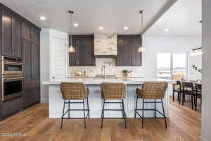 Kitchen with light hardwood / wood-style floors, dark brown cabinetry, stainless steel double oven, and a kitchen island with sink