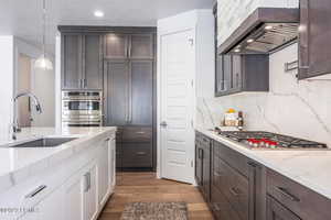 Kitchen with sink, hanging light fixtures, dark wood-type flooring, wall chimney range hood, and white cabinets