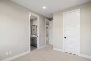 Unfurnished bedroom featuring ensuite bathroom, light colored carpet, and sink