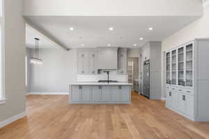 Kitchen with a large island with sink, gray cabinets, light hardwood / wood-style floors, and stainless steel built in refrigerator