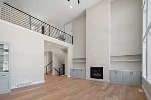 Unfurnished living room featuring a wealth of natural light, ceiling fan, light wood-type flooring, and a high ceiling