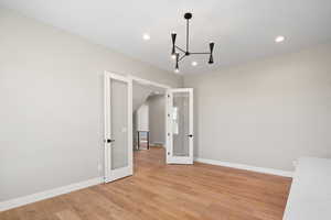 Unfurnished room featuring a notable chandelier, light hardwood / wood-style floors, and french doors