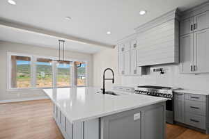 Kitchen with high end stove, sink, an island with sink, and light hardwood / wood-style flooring