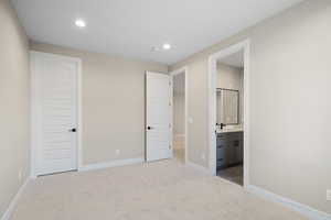 Unfurnished bedroom with ensuite bathroom and light colored carpet