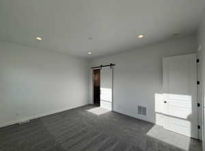 Unfurnished bedroom with a barn door and dark carpet