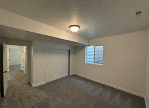 Unfurnished bedroom featuring dark carpet, a textured ceiling, and a closet