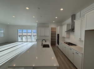 Kitchen with a large island, sink, wall chimney exhaust hood, stainless steel appliances, and dark wood-type flooring