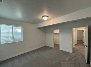 Unfurnished bedroom featuring dark colored carpet, a walk in closet, a textured ceiling, and a closet