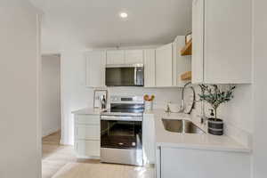 Kitchen with white cabinets, sink, stainless steel appliances, and light hardwood / wood-style flooring