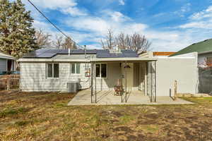 Back of property with a yard, cooling unit, a patio, and solar panels