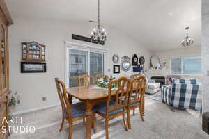 Dining room with a tiled fireplace, light carpet, vaulted ceiling, and a notable chandelier