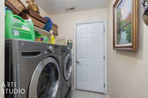 Laundry area with a textured ceiling, washing machine and dryer, and light tile patterned flooring