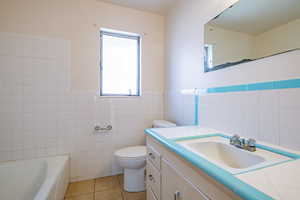 Bathroom with tile patterned flooring, a tub to relax in, toilet, vanity, and tile walls