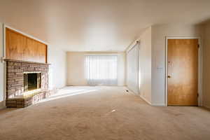 Unfurnished living room featuring a stone fireplace and light carpet