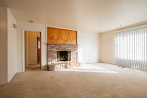 Unfurnished living room featuring a stone fireplace and light colored carpet